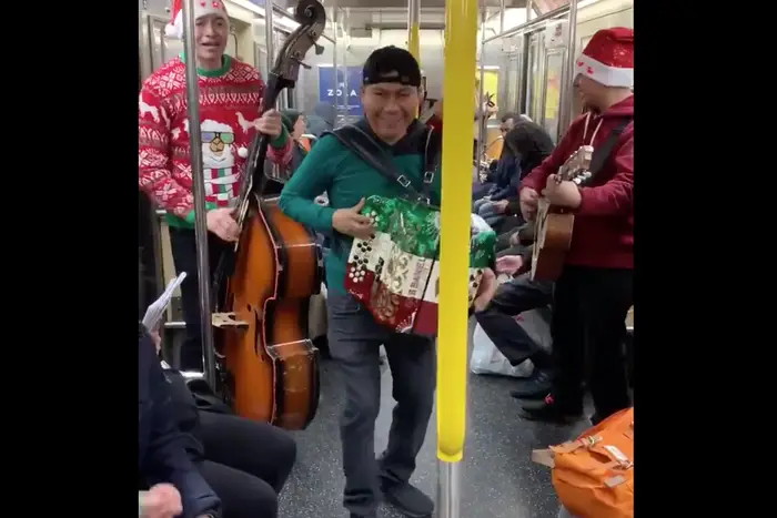 A mariachi band plays "Feliz Navidad" while wearing Christmas sweaters and Santa hats on the 1 train.